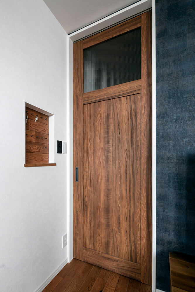 玄関とリビングの仕切り扉は、天井までのハイドア。リビング側の壁に造作したニッチは便利な鍵置き場に