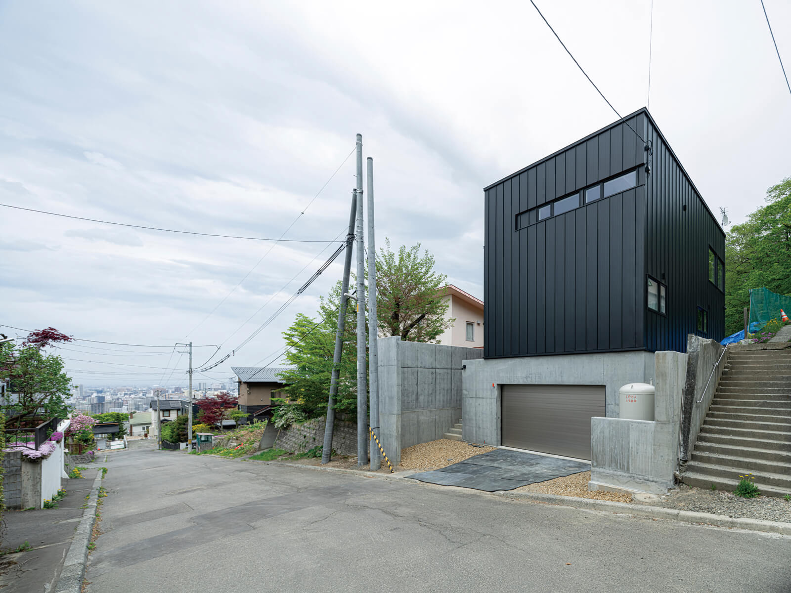 高台にある閑静な住宅地でひと際目を引く黒のガルバリウム鋼板とコンクリートの外観